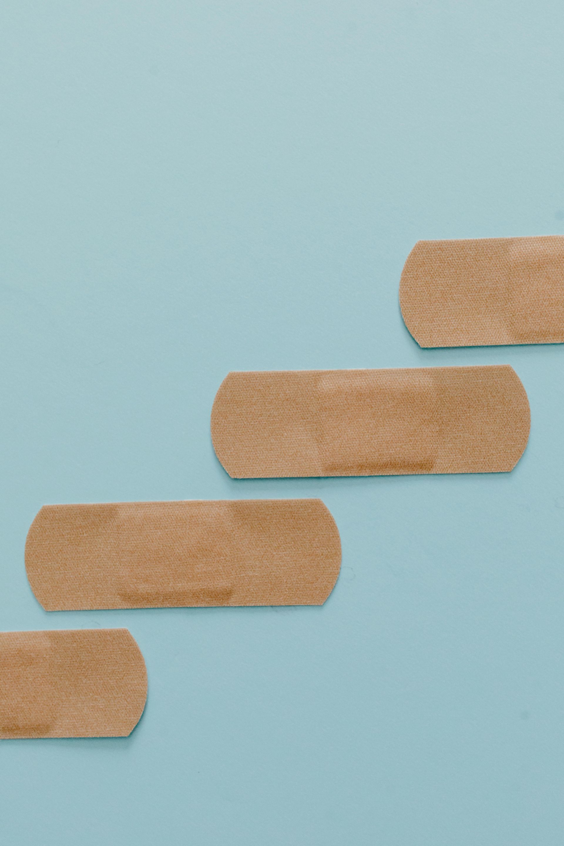 Four tan bandages arranged diagonally on a light blue background.
