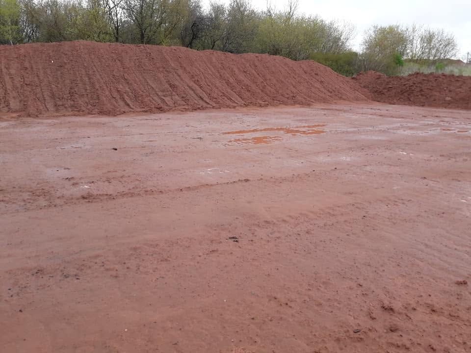 Wet dirt lot with a large mound of red soil under an overcast sky