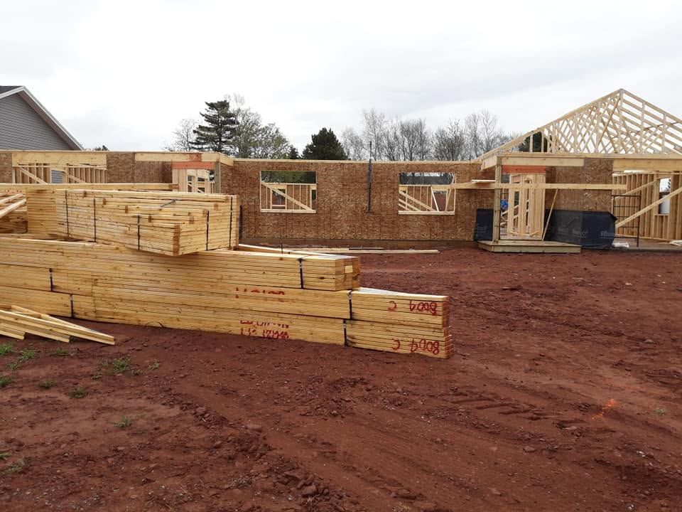 Partially built wooden house framing on a muddy construction site under an overcast sky