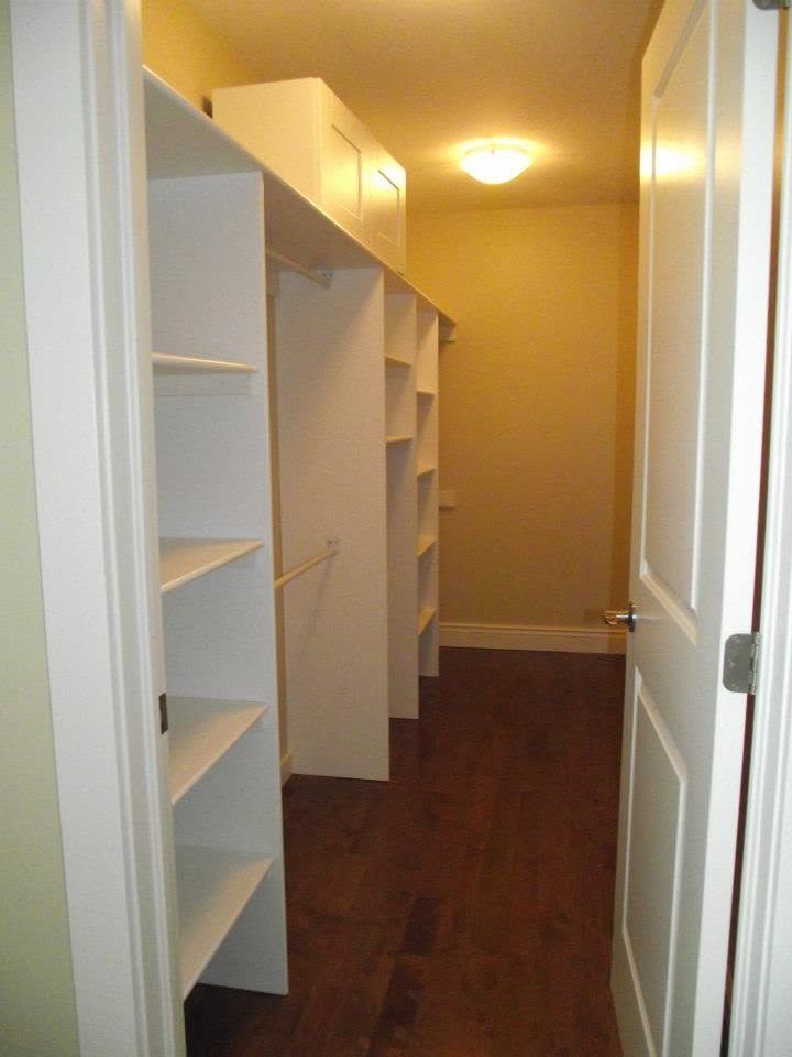 Narrow walk-in closet with white shelving and dark wood floor under warm ceiling light.