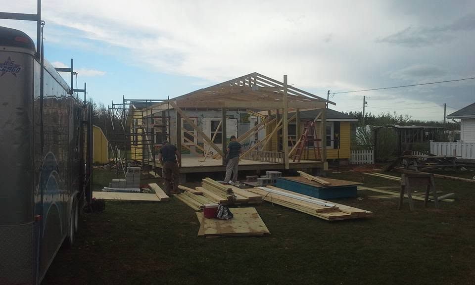 Partly built wooden house frame at a construction site with tools, ladders, and materials scattered around