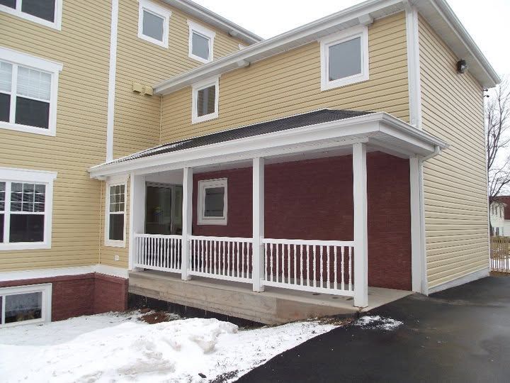 Snowy townhouse entrance with covered porch, white railings, and red and beige siding