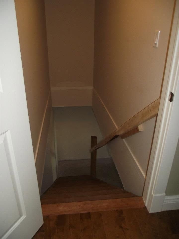 Narrow basement stairwell with beige walls, wooden steps, and a handrail at the landing