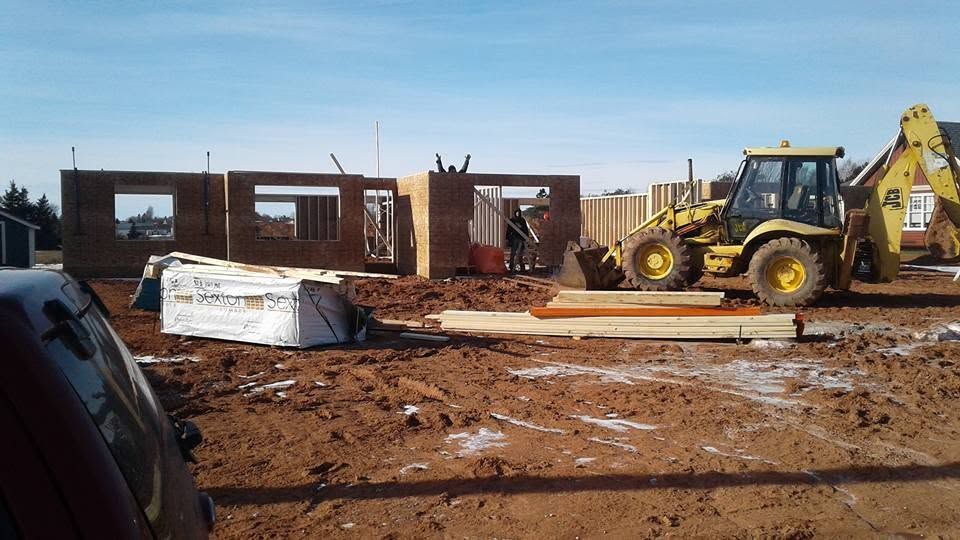 Construction site with a yellow backhoe near unfinished brick buildings and muddy ground