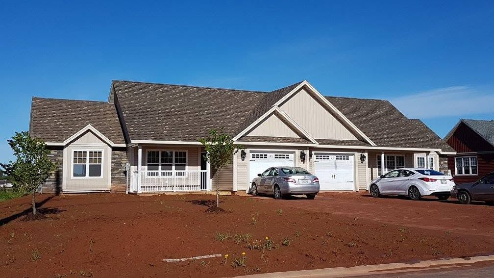 Single-story suburban house with a tiled roof, red dirt front yard, and two parked cars under a blue sky