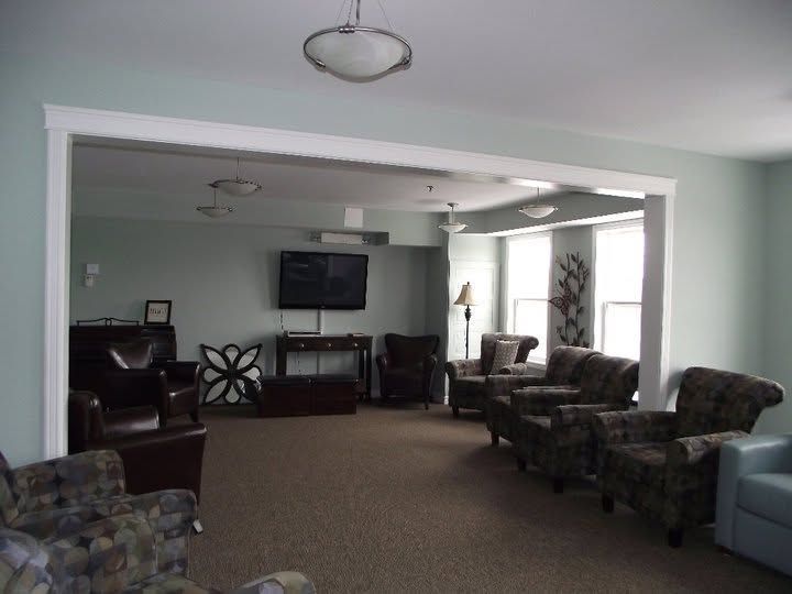 Spacious living room with patterned armchairs, a wall-mounted TV, and open doorway to a dining area.