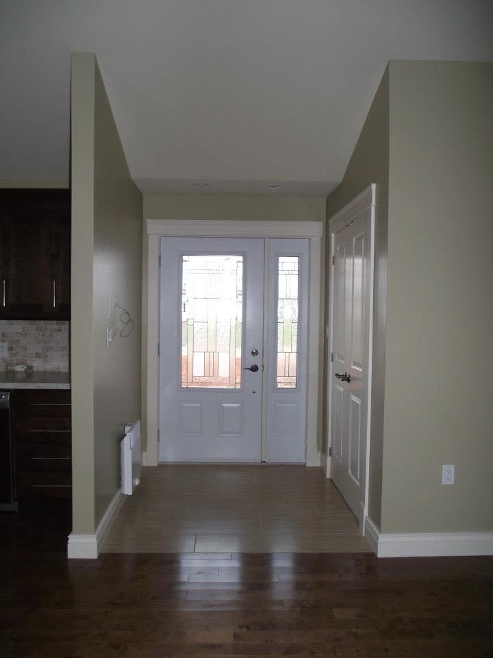 Empty entryway with hardwood floors, tan walls, and white front door with sidelights.