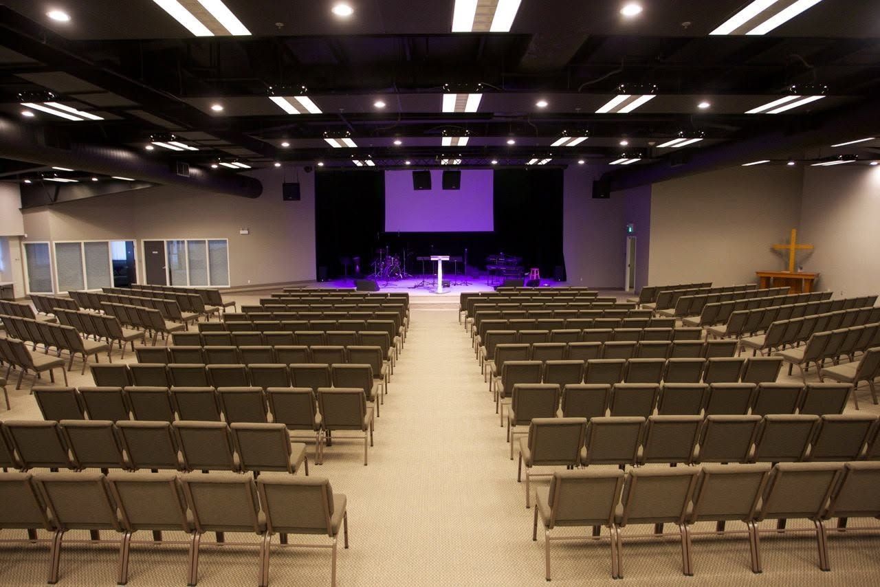 Empty auditorium with rows of chairs facing a lit stage and projection screen