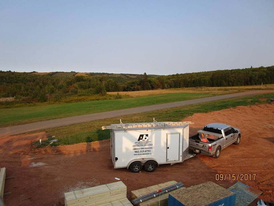 Truck towing a white utility trailer on a dirt lot beside a road and grassy field under clear sky