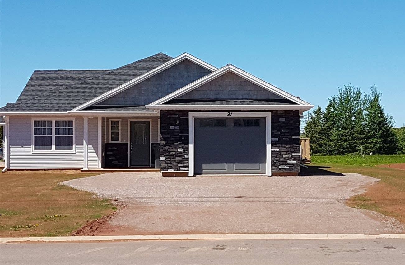 Single-story suburban house with gray roof, attached garage, and wide driveway on a sunny day