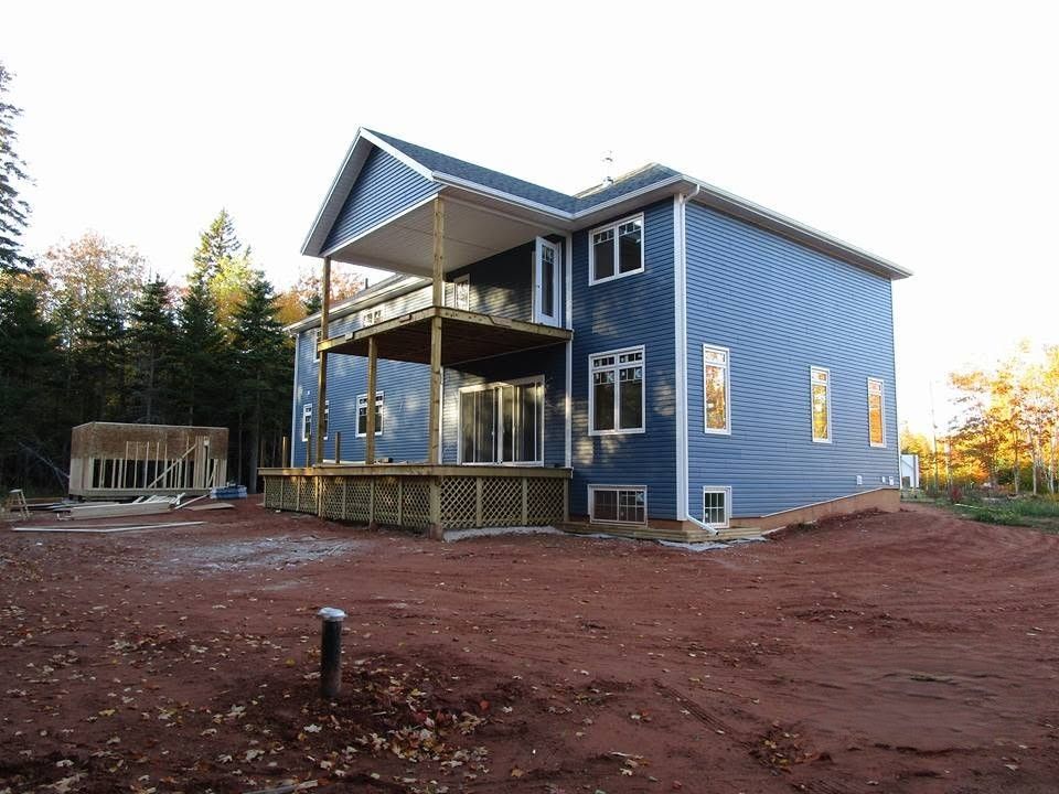 Blue two-story house with a covered porch on bare red dirt, surrounded by trees