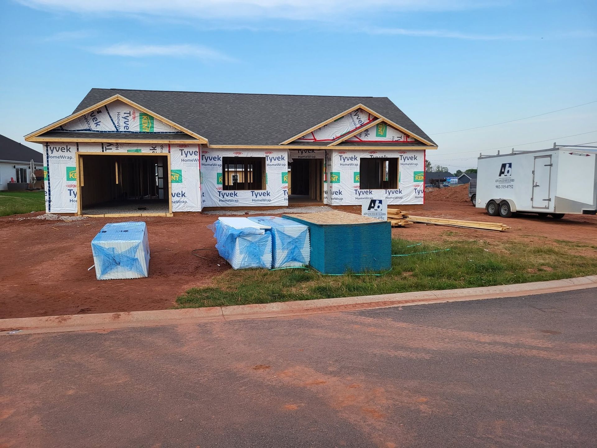 Small white building with open bays and blue-covered crates on a dirt lot beside a road