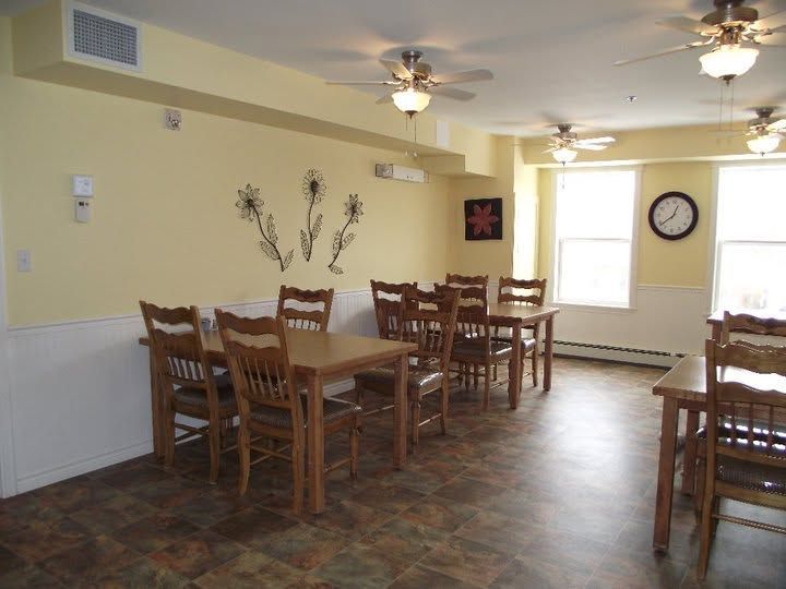 Dining room with wooden tables and chairs, beige walls, ceiling fans, and a bright window.