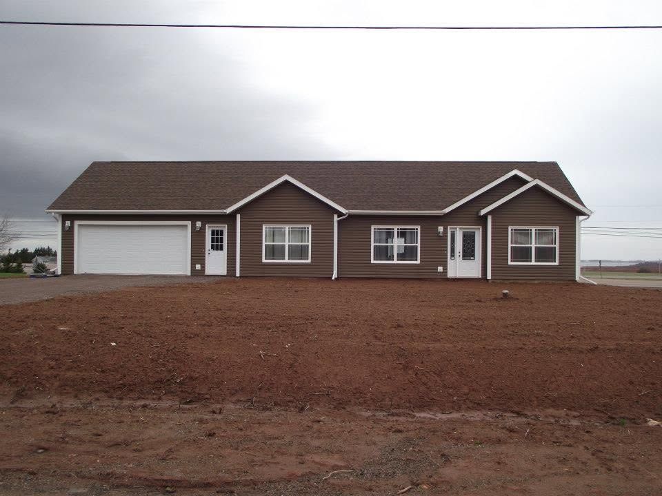 Single-story brown house with white trim on a bare dirt lot under a cloudy sky.