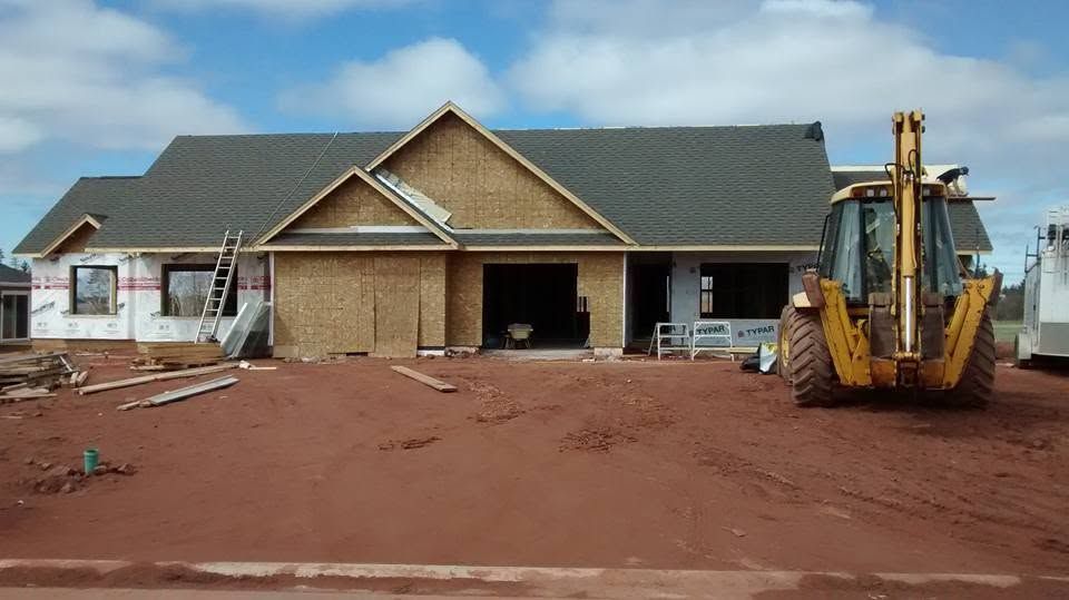 New house under construction with a yellow backhoe on a red dirt lot