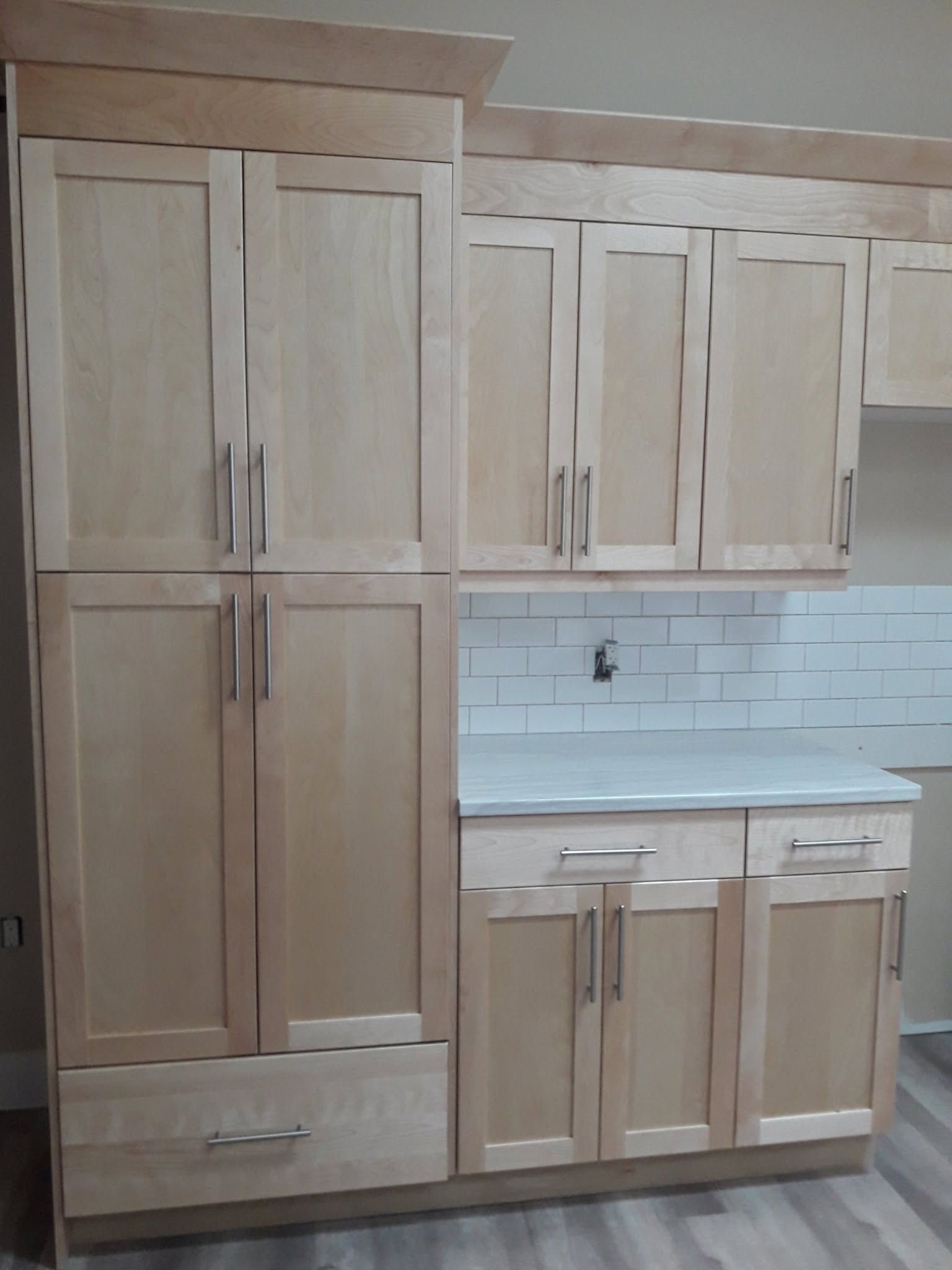 Light wood kitchen cabinets with white countertop and tiled backsplash in a small kitchen