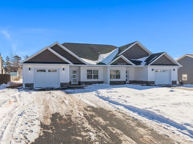 Snowy suburban house with two garages and a dark roof under a clear blue sky