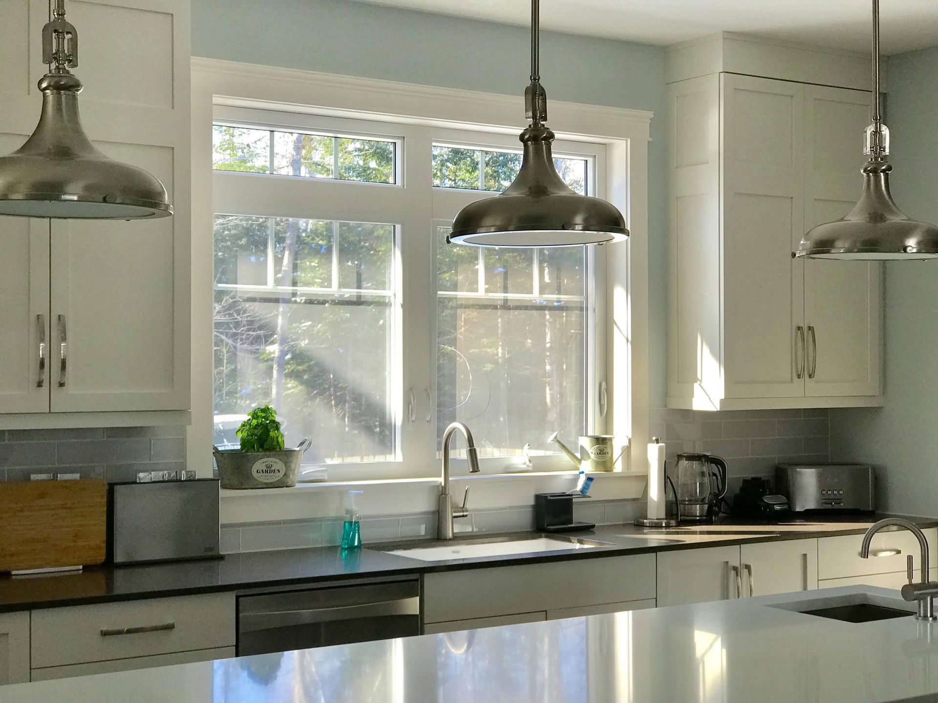 Bright kitchen with white cabinets, large window, pendant lights, and a countertop sink.