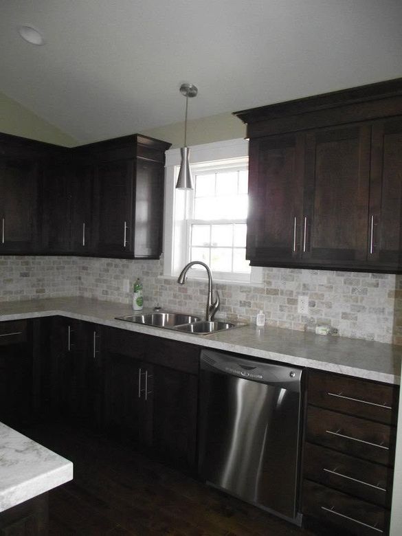 Modern kitchen with dark cabinets, stainless steel dishwasher, and a window over the sink