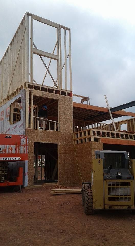Construction site with a tall wooden building frame and a yellow skid-steer loader on dirt ground.