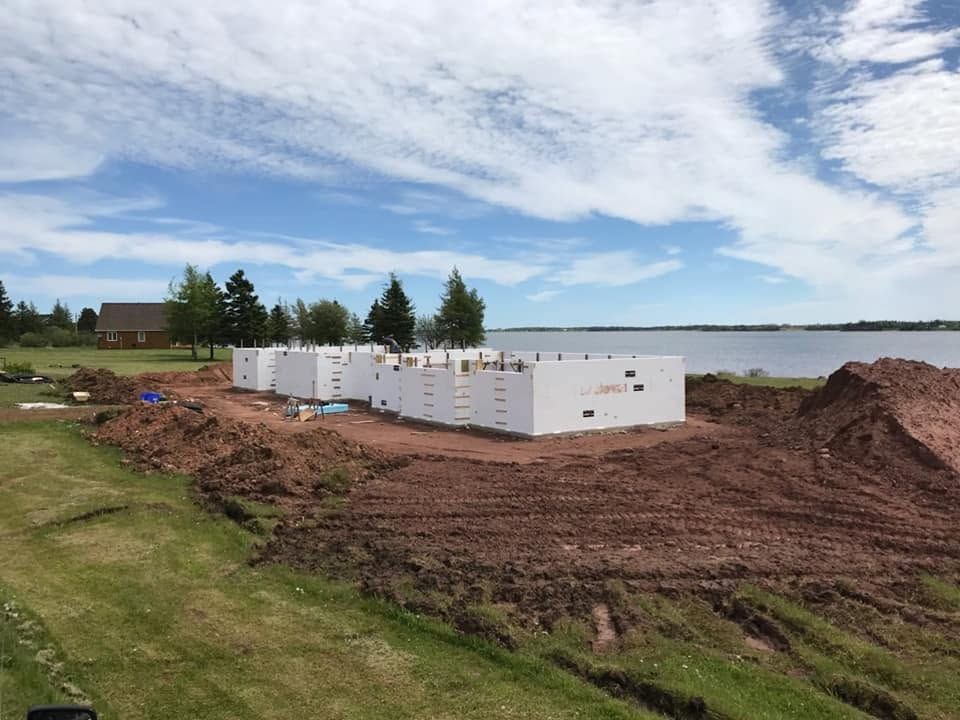 White utility containers on a dirt lot by a lake under a cloudy sky