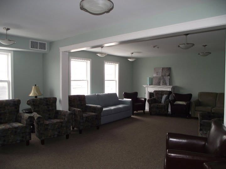Quiet living room with several armchairs, a sofa, and a fireplace beneath tall windows.