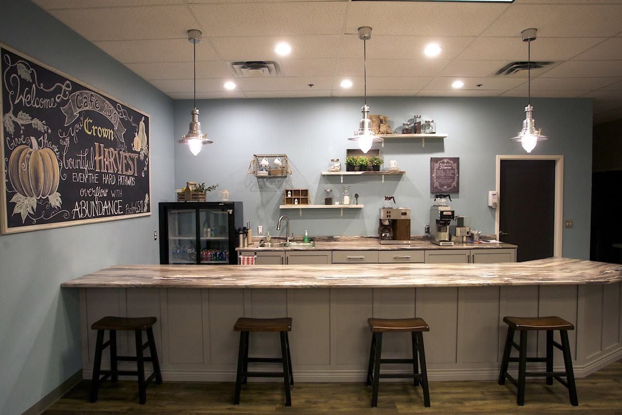 Empty café counter with four stools, pendant lights, and shelves against a light gray wall