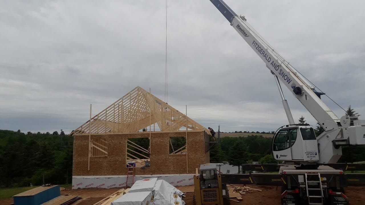 Partially built wooden house with a crane on a construction site under a cloudy sky