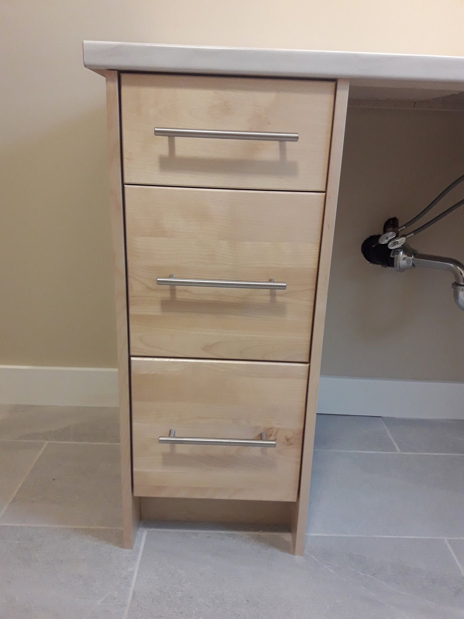 Small wooden cabinet with three drawers under a countertop in a tiled bathroom or kitchen.