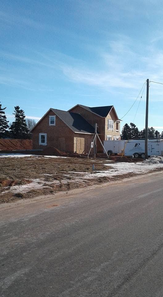 Small brick house and white building beside a snowy roadside under a blue sky