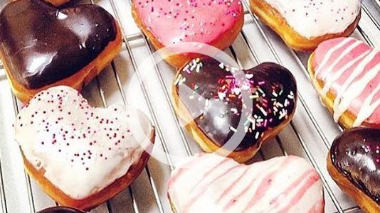 A bunch of heart shaped donuts are sitting on a cooling rack.