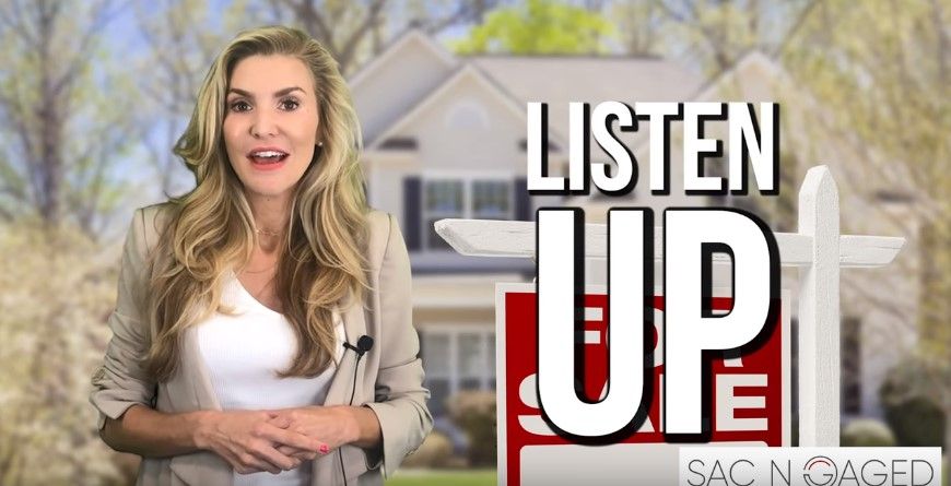 A woman is standing in front of a house with a sign that says listen up.