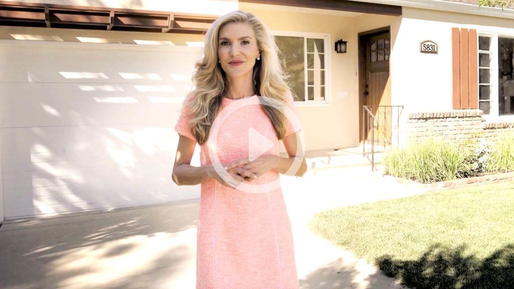 A woman in a pink dress is standing in front of a house.