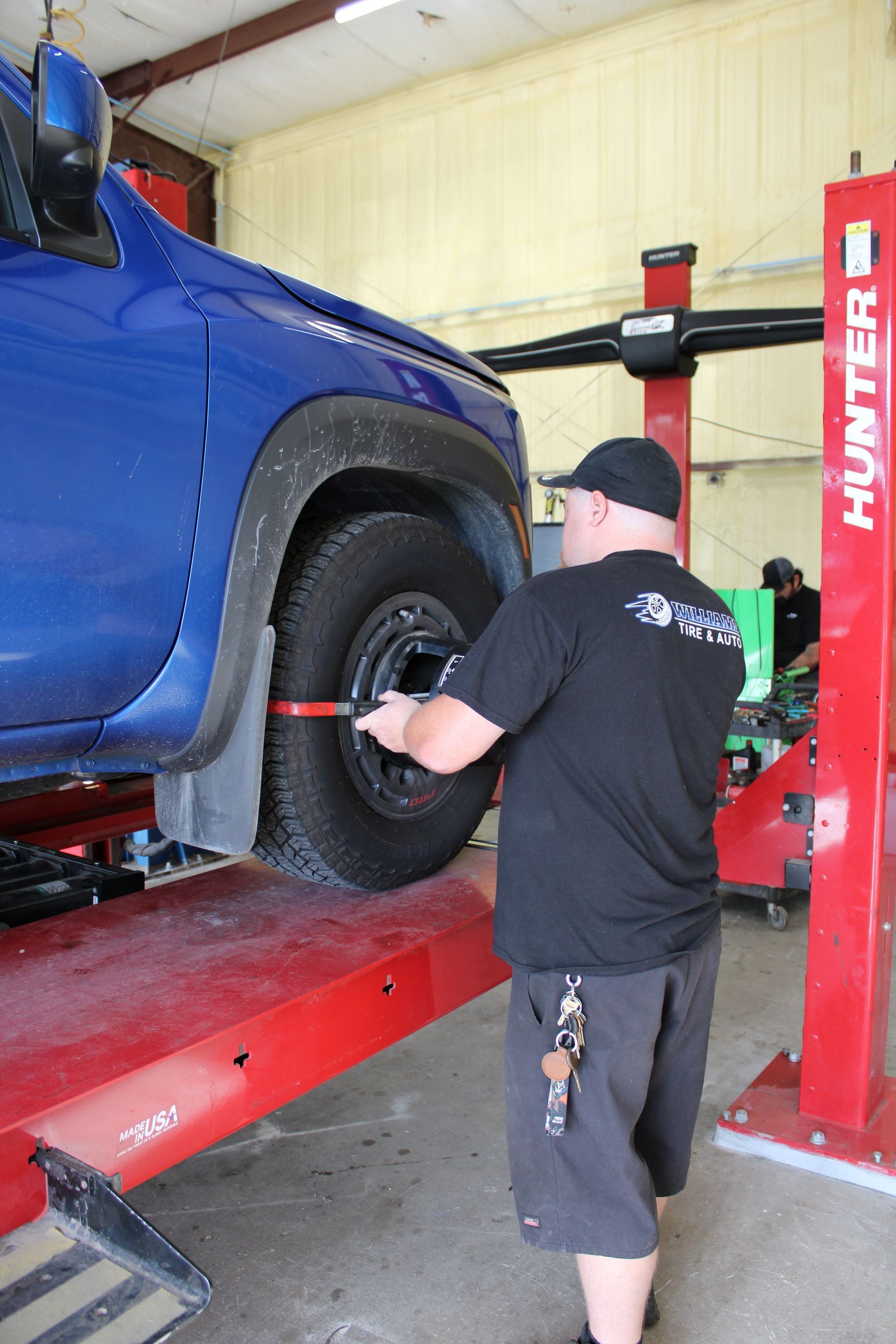 Mechanic adjusting a blue truck’s front wheel on a red lift in a garage