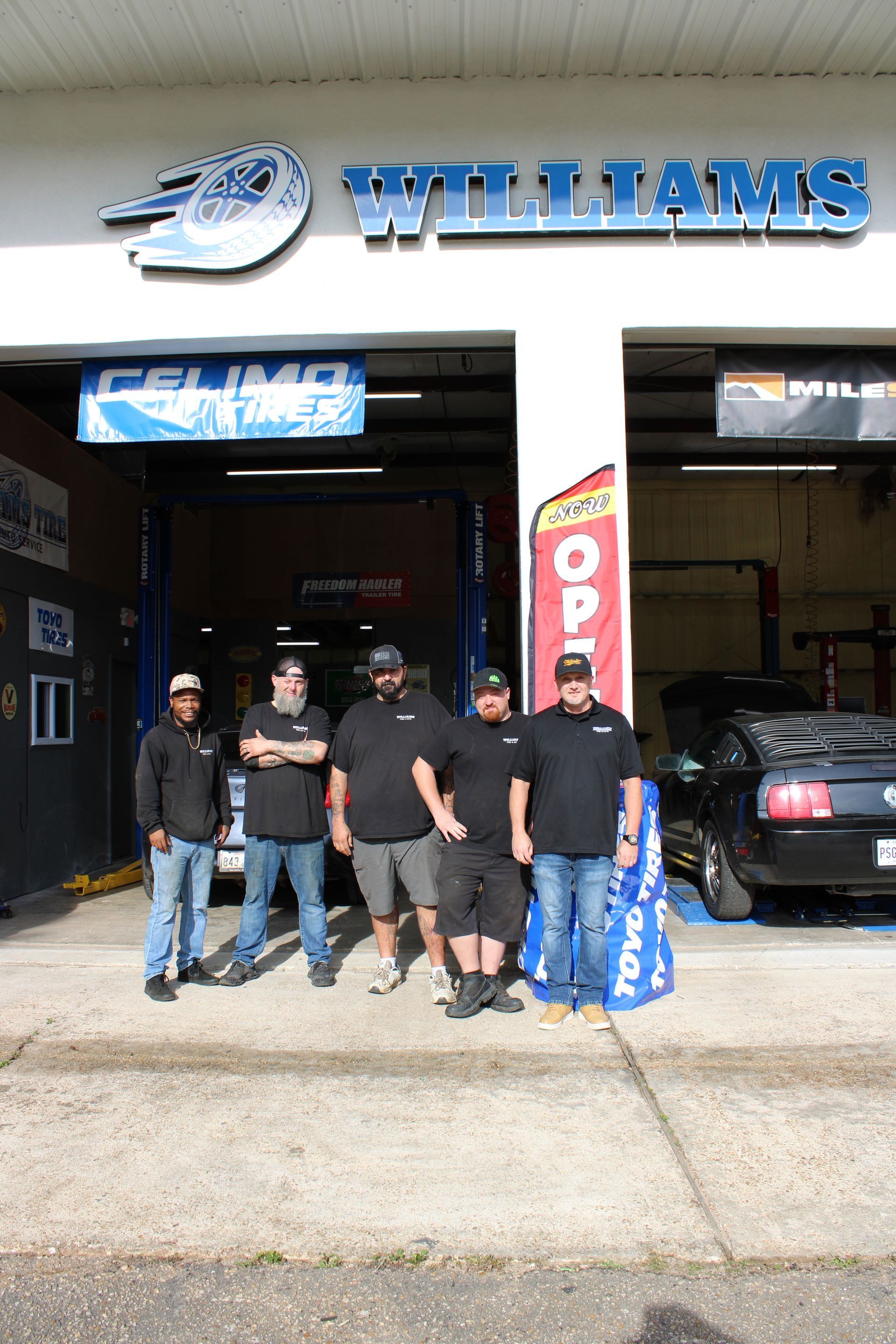 Four people posing outside Williams auto shop with an open garage door and a car inside