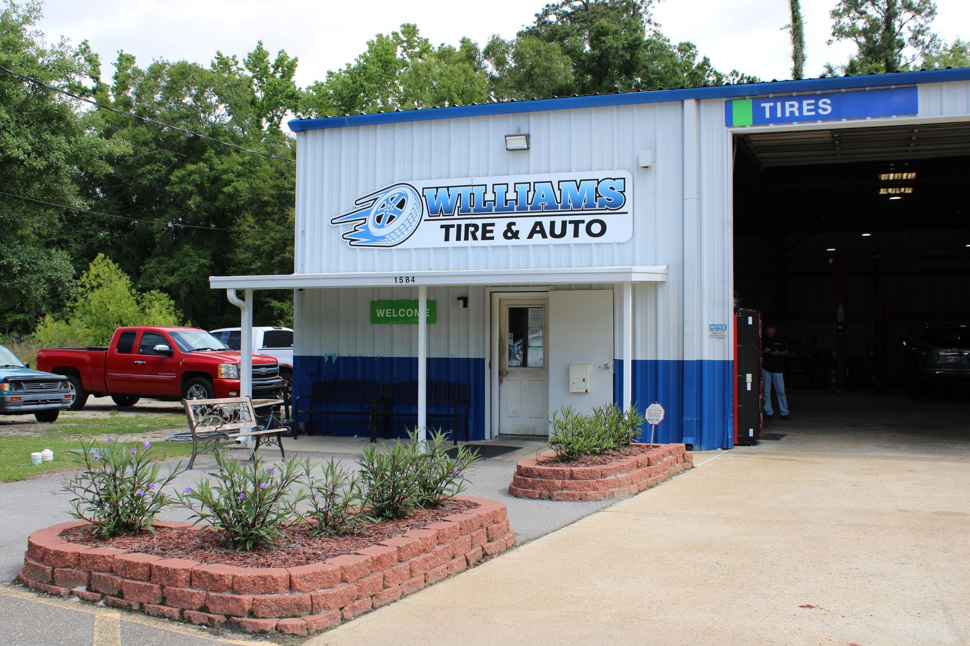 Exterior of a tire and auto shop with blue trim, a red truck parked outside, and an open garage bay