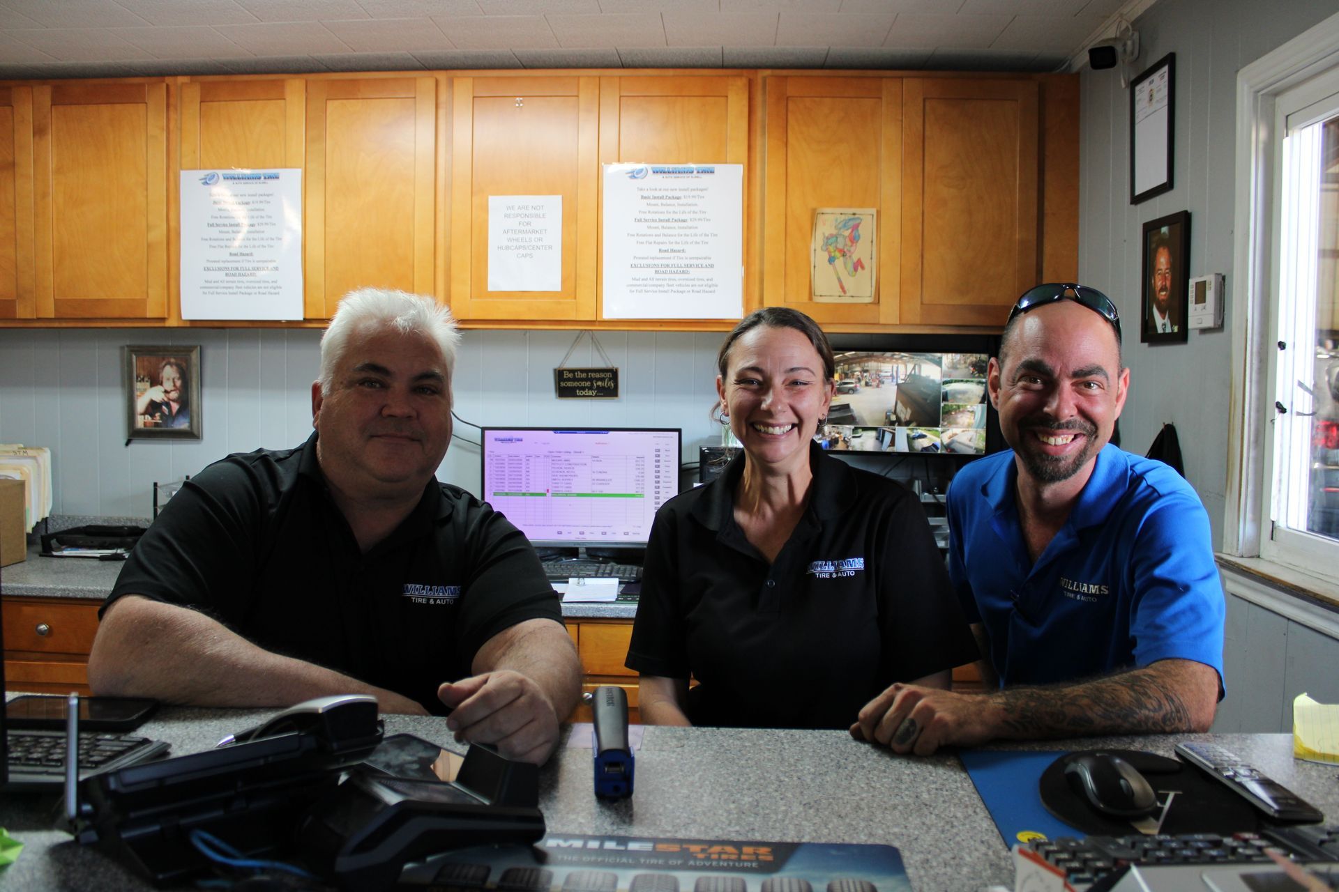 Three people smiling behind a desk in an office with wood cabinets and papers on the wall