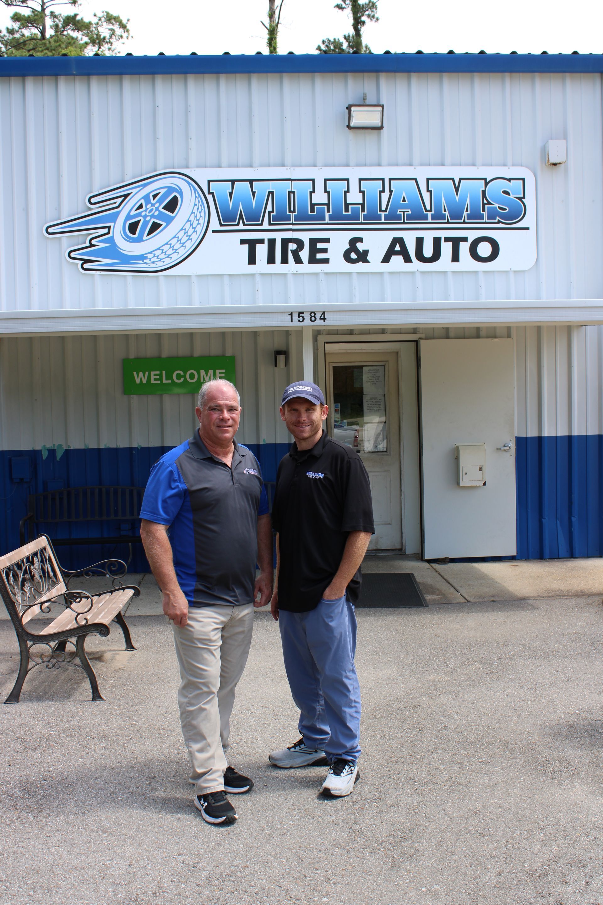 Two men standing outside Williams Tire & Auto in front of the storefront sign