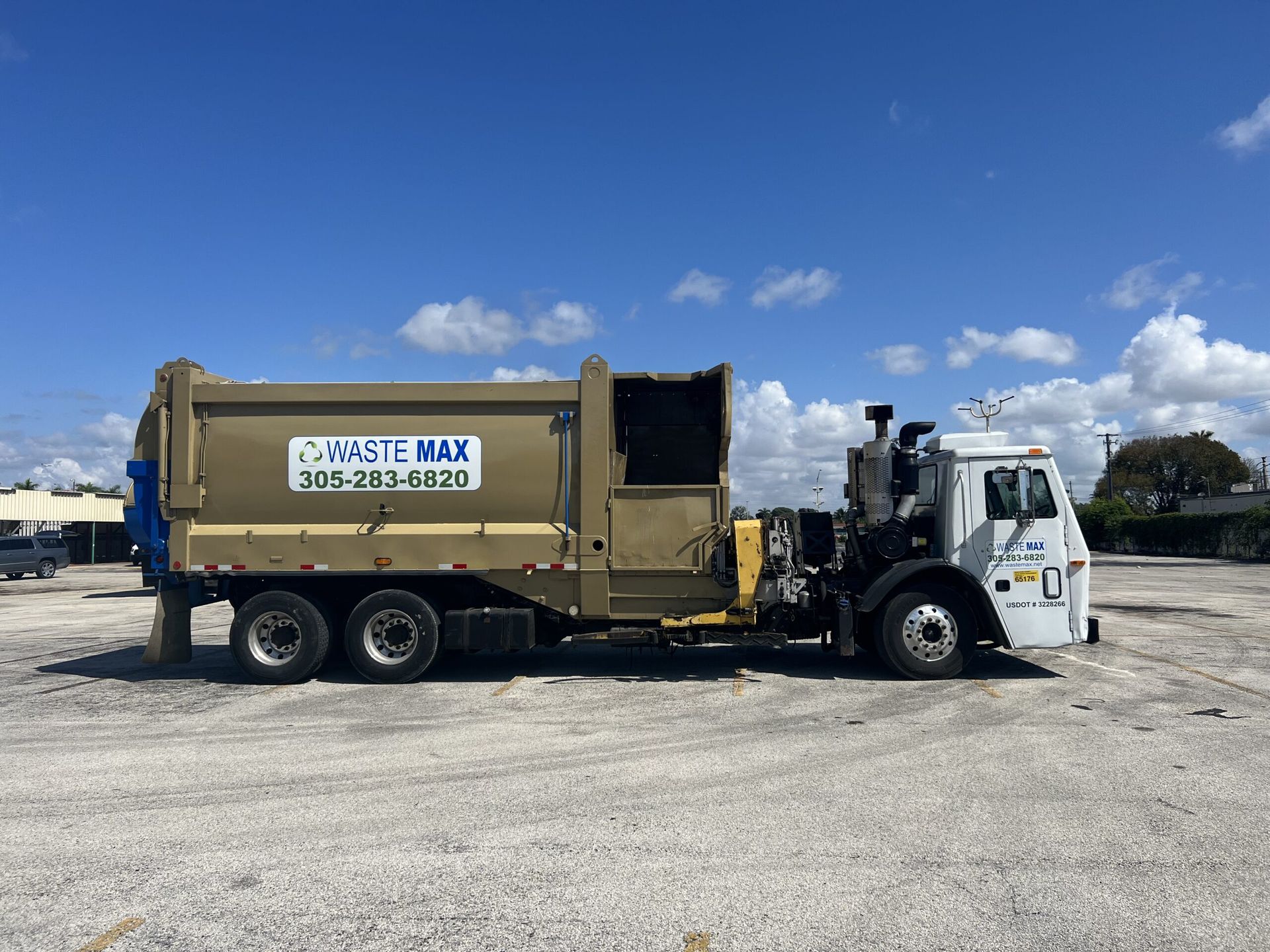 A garbage truck is parked in a parking lot on a sunny day.
