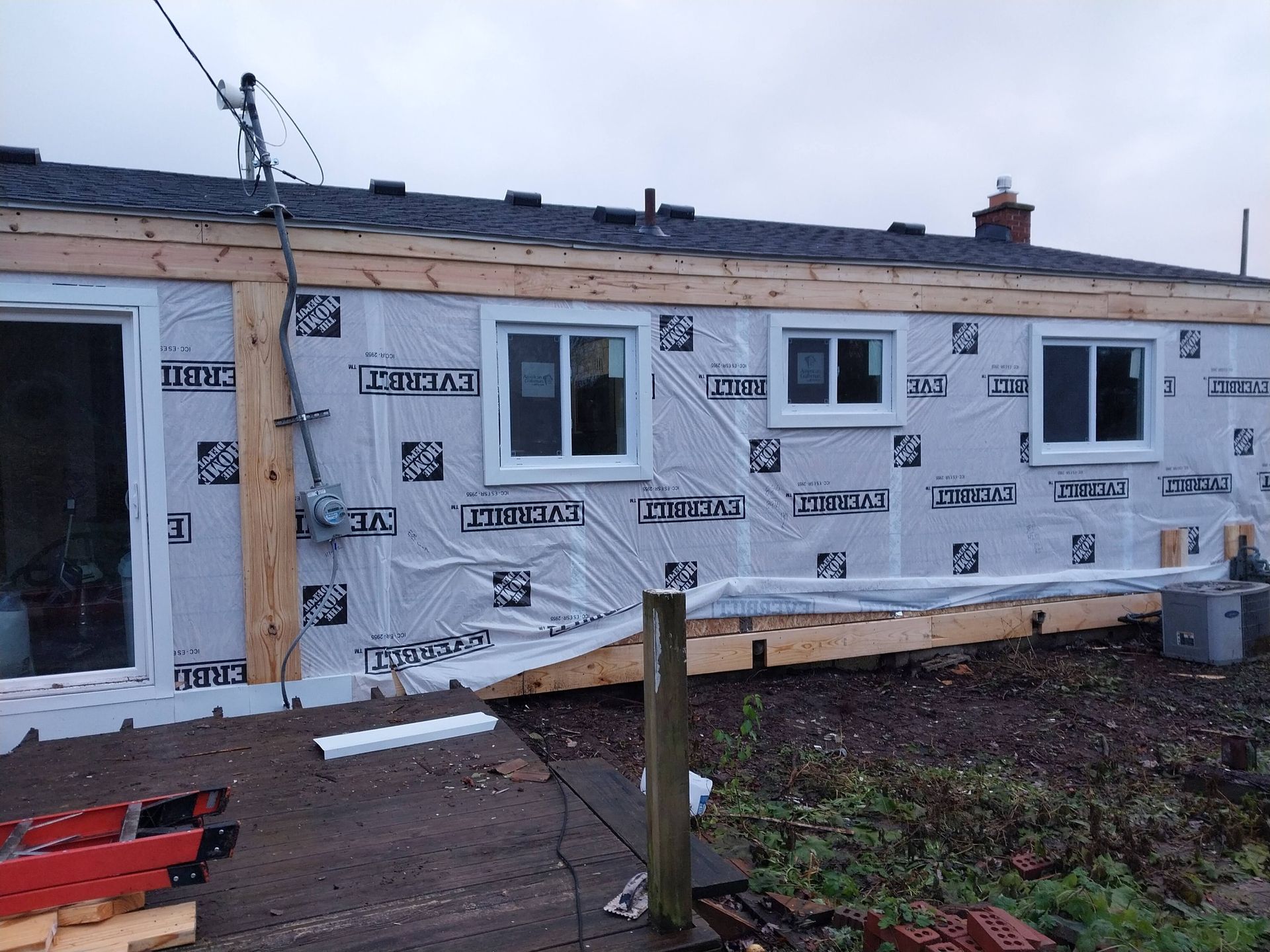 House exterior under renovation, wrapped in white insulation and plywood framing around windows and door.