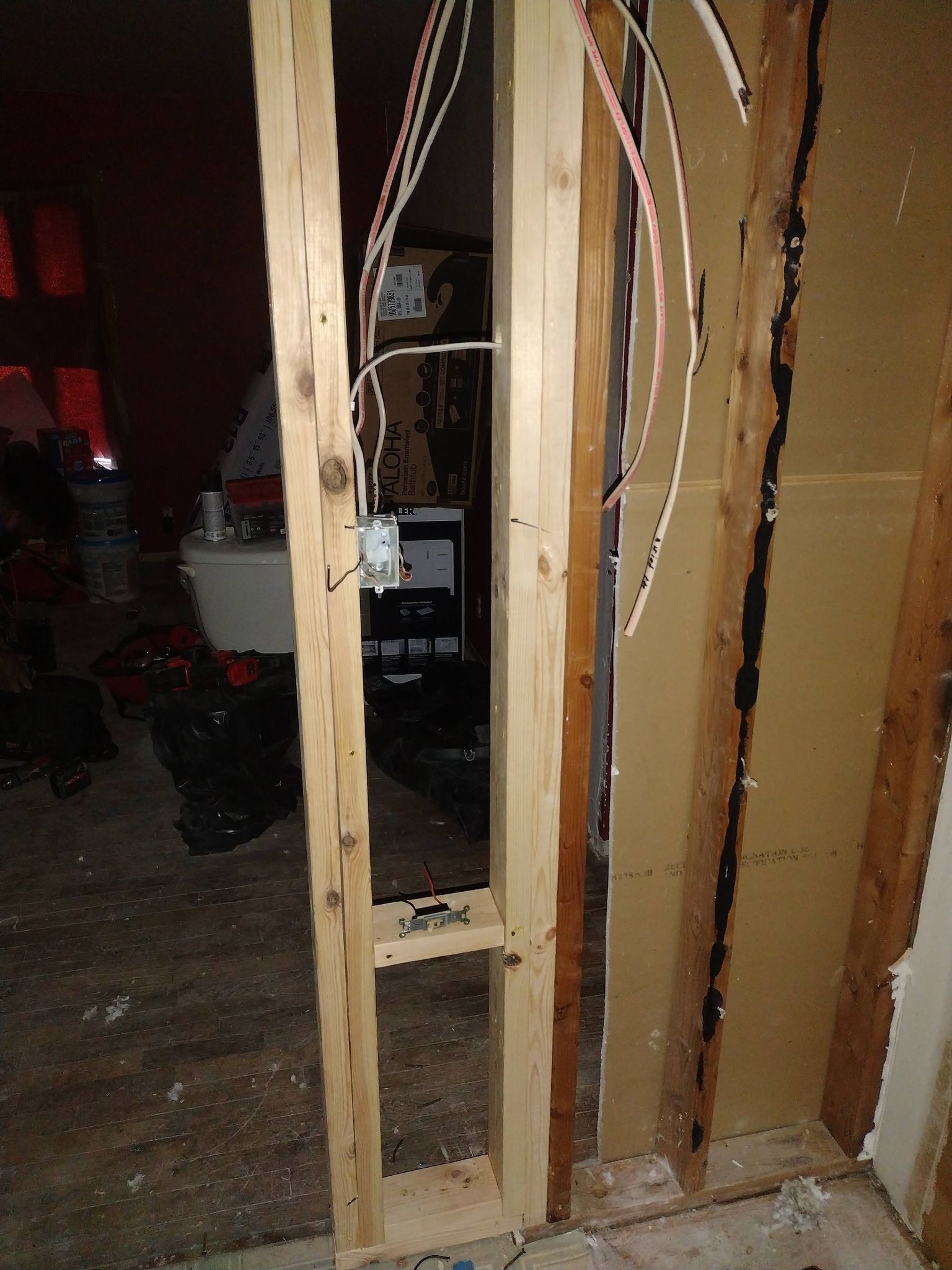 Damaged interior wall framing with exposed studs and wiring in a dim room