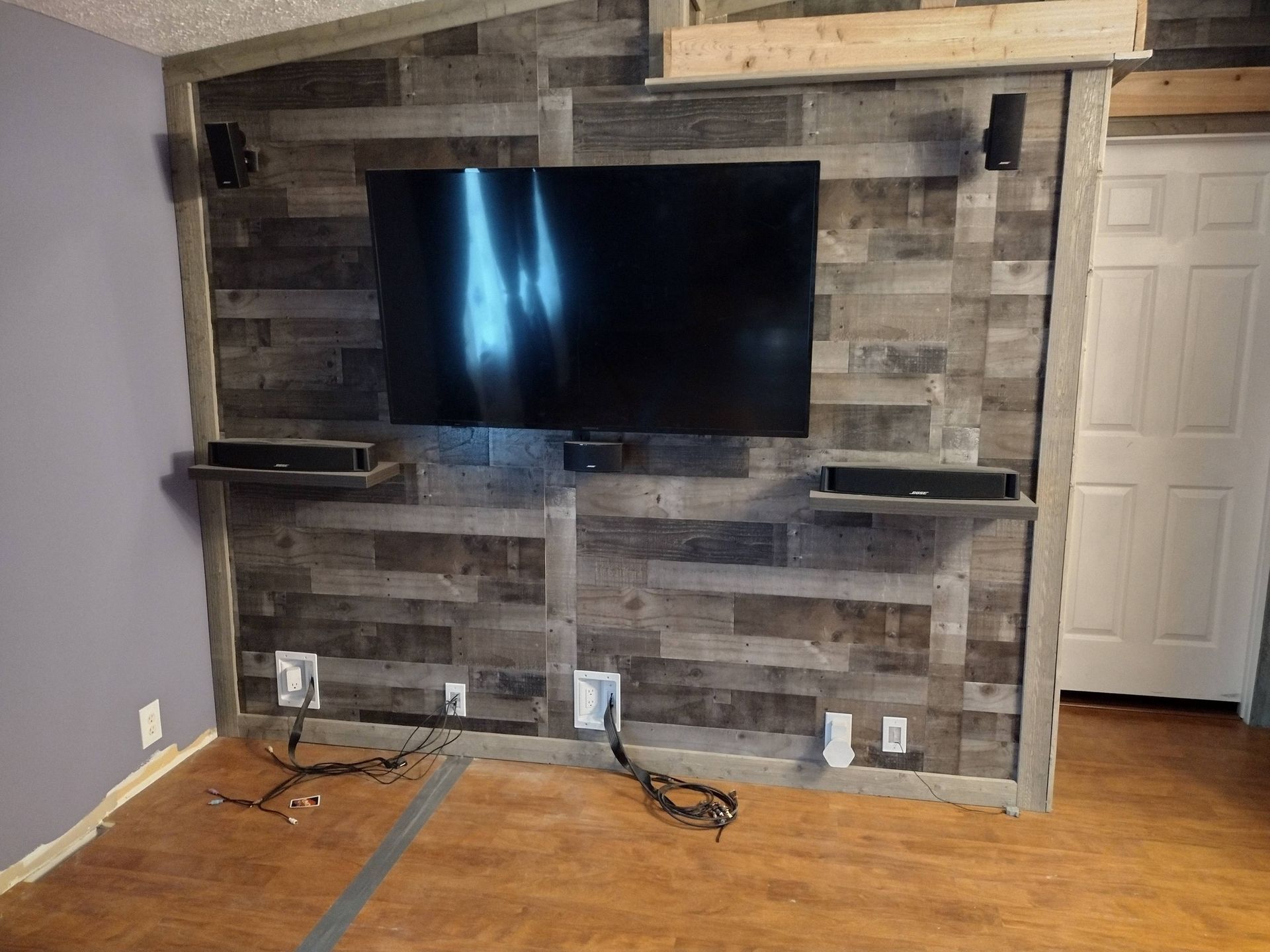 Living room wall with a large TV mounted on rustic wood and stone paneling above built-in shelves.