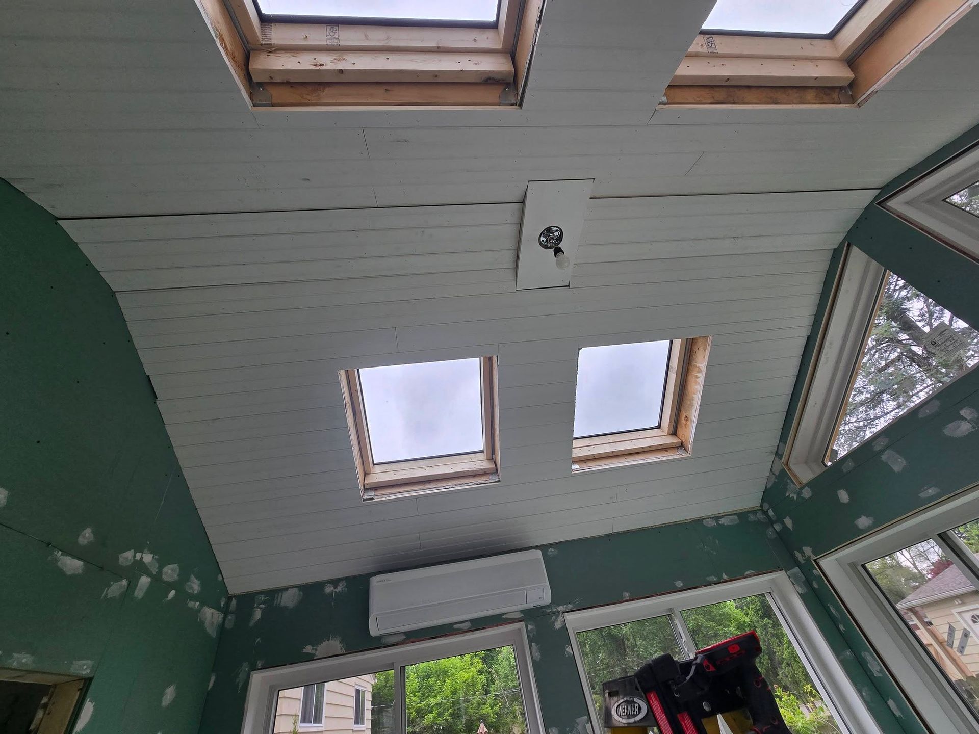 Green porch ceiling with skylights, two small windows, and a hanging light fixture above glass doors.
