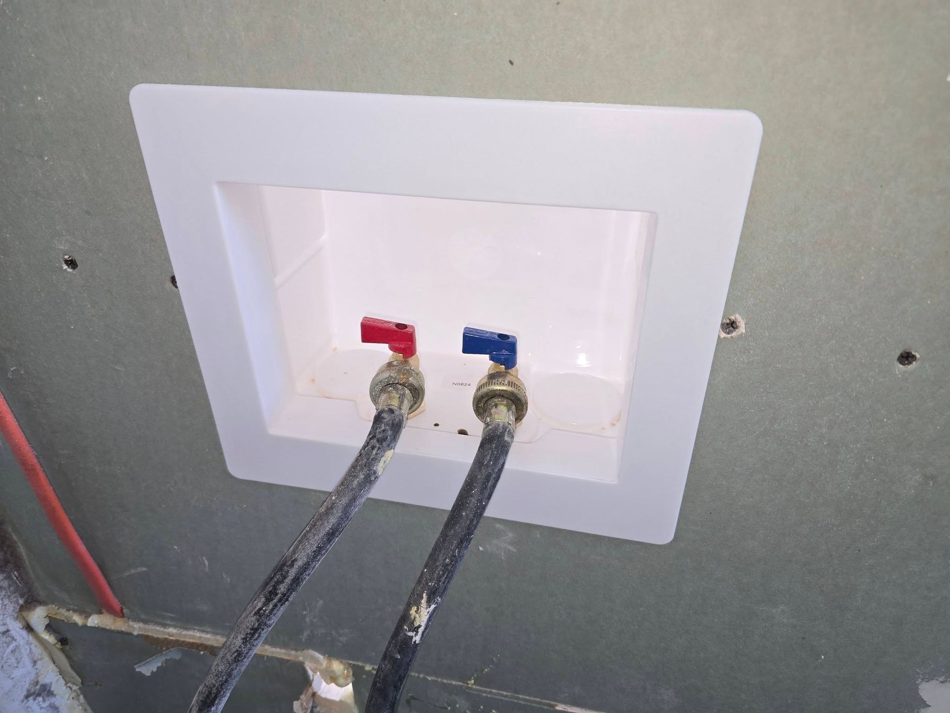 Two wall-mounted hose connections with red and blue valves inside a recessed white utility box