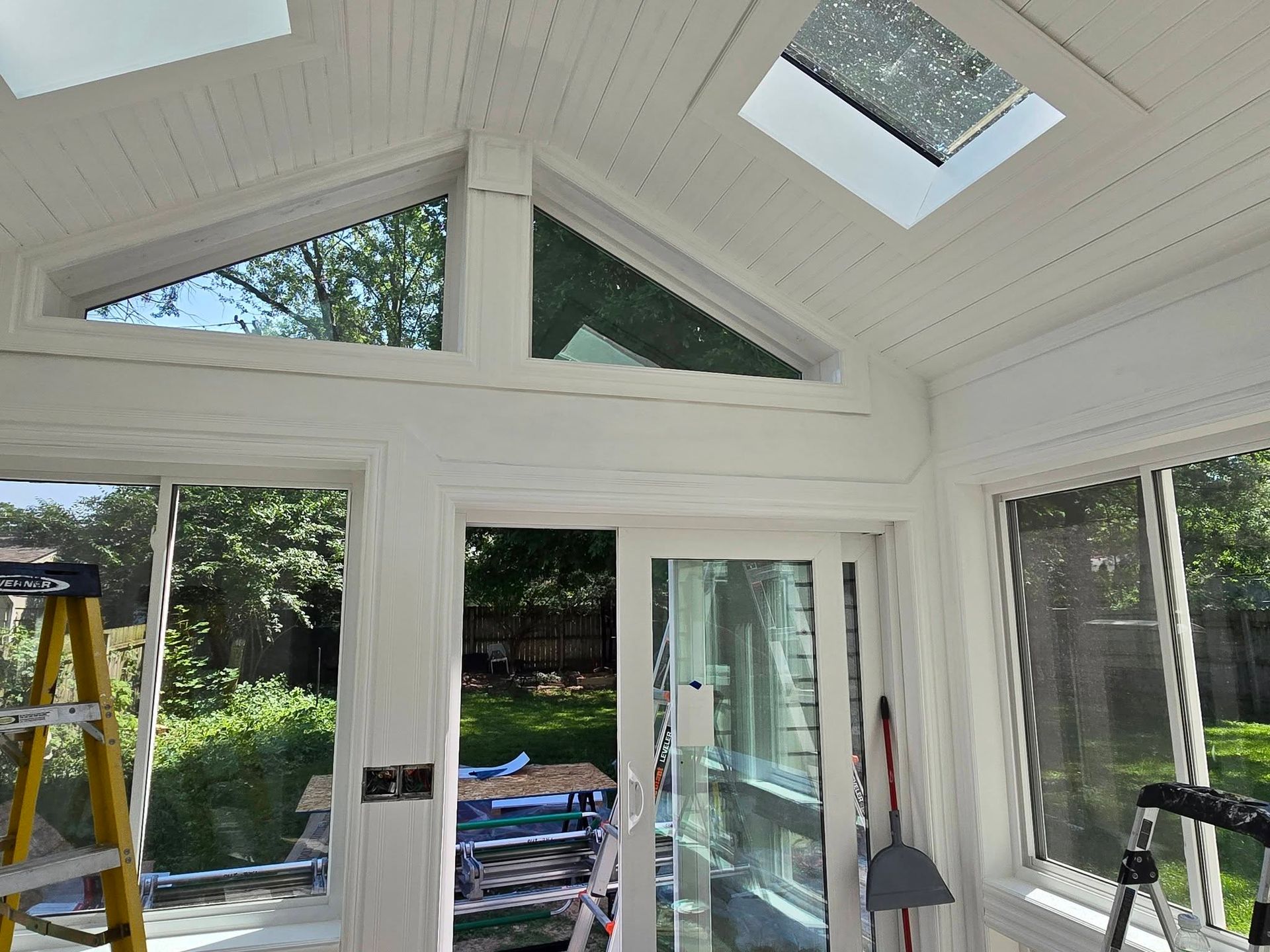 Bright sunroom with white vaulted ceiling, skylights, glass doors, and a ladder near the entrance.
