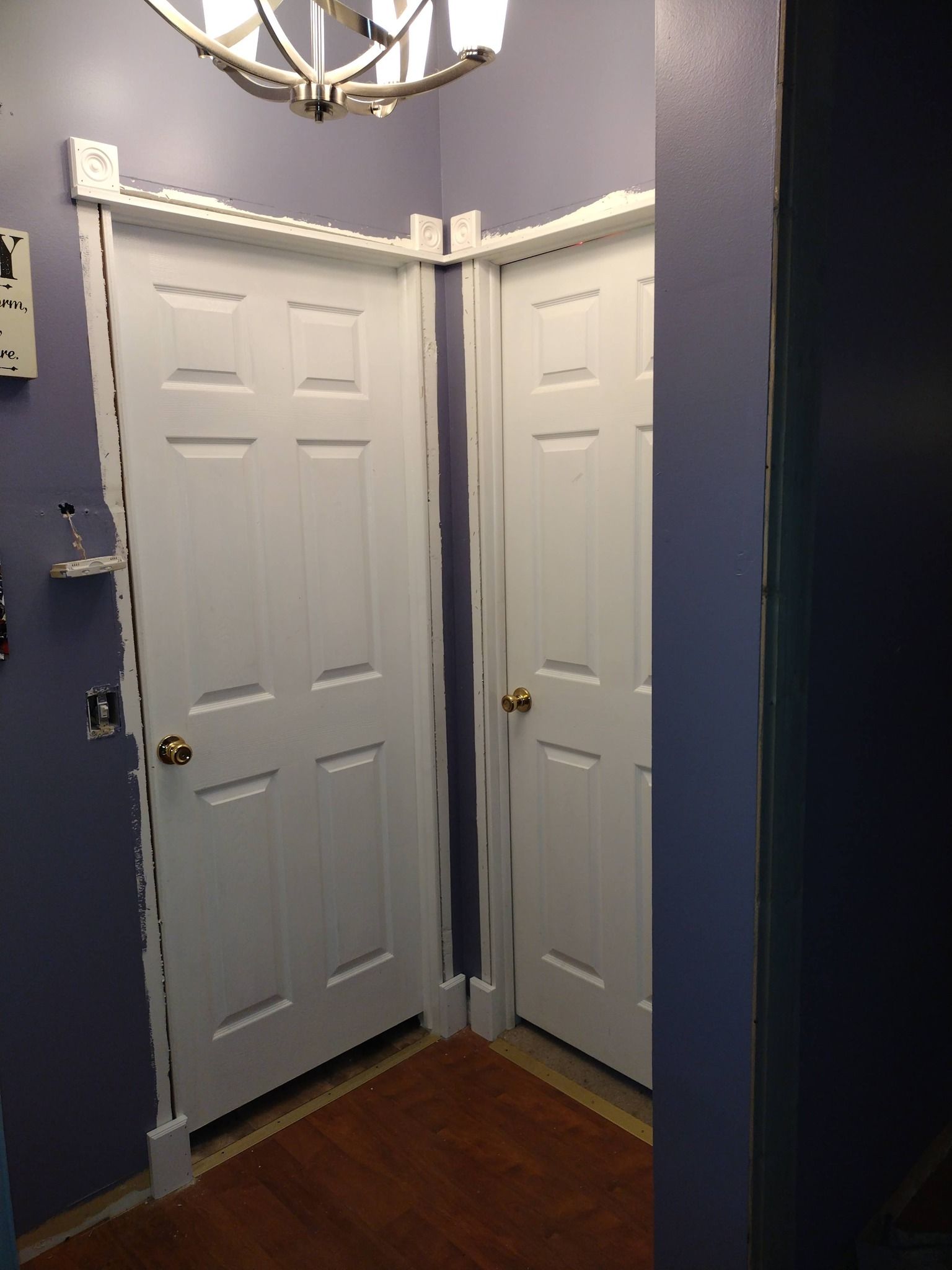 Two white interior doors meet in a corner with dark blue walls and hardwood floor.