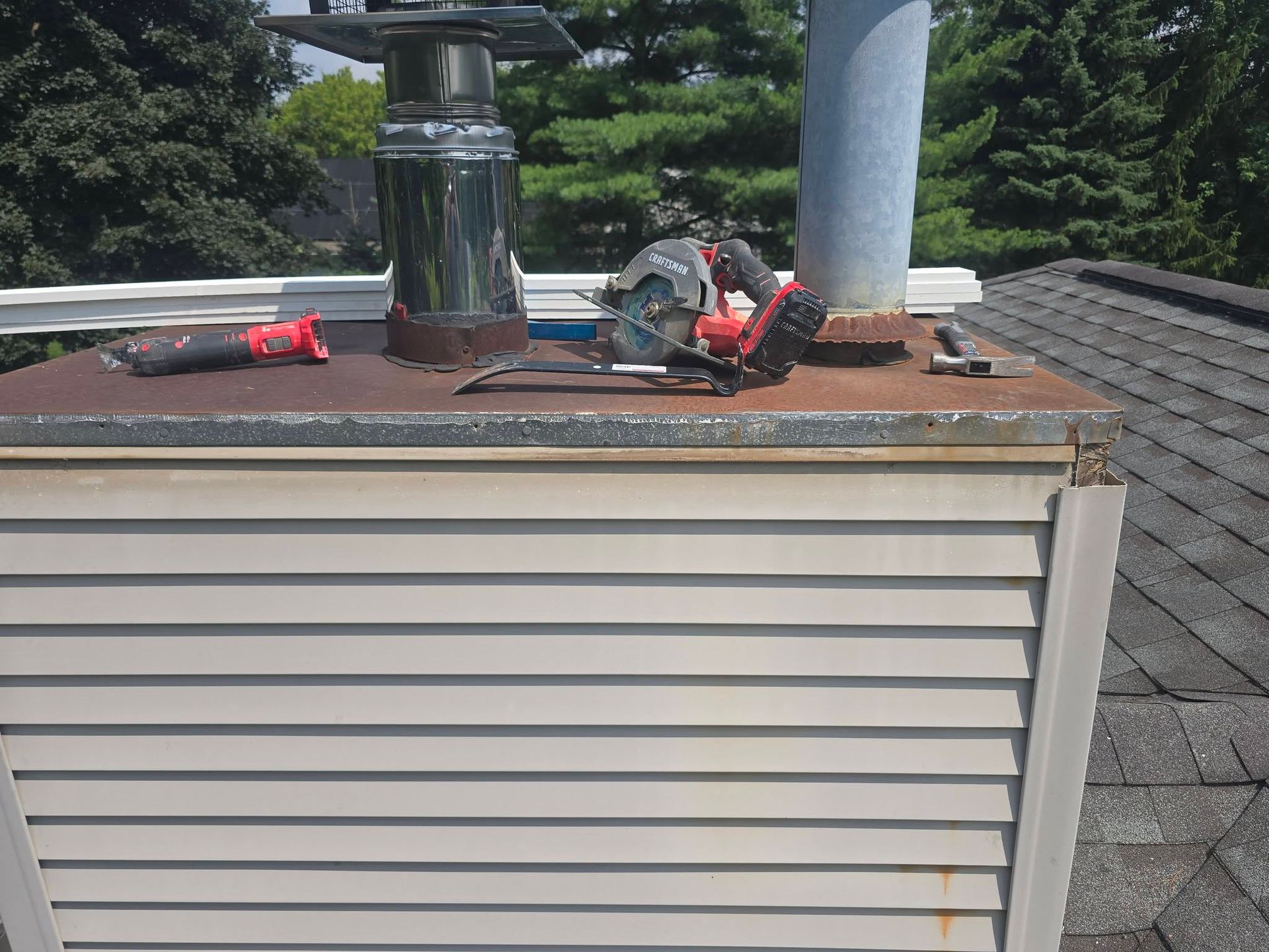 Roof with a rusted HVAC unit, metal vent pipes, and tools on top of a beige-sided building