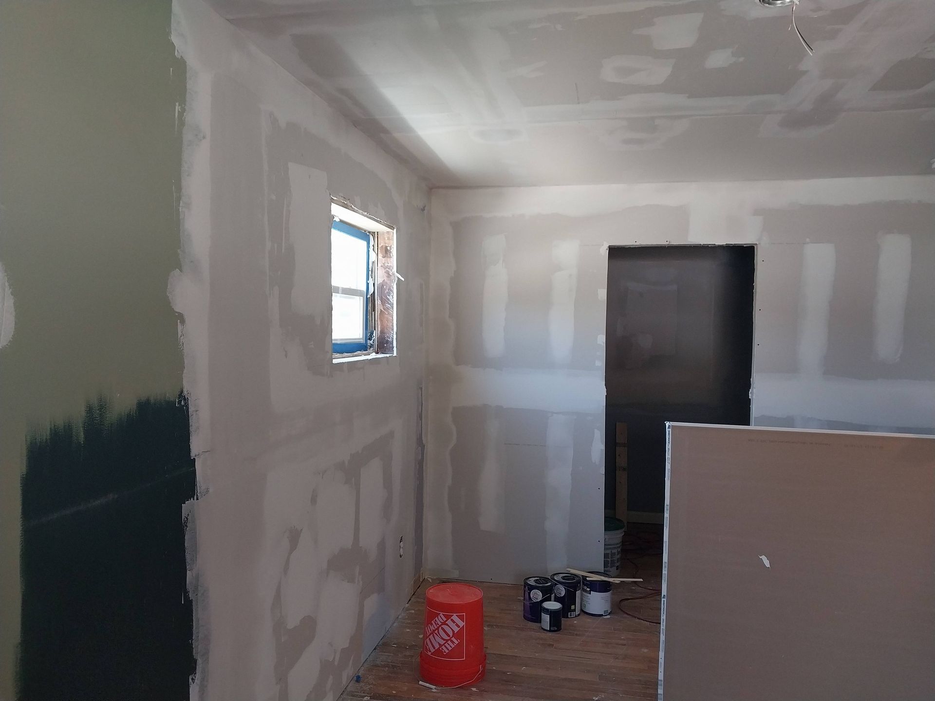 Partially finished room with white drywall, a small window, dark door, and construction supplies on the floor