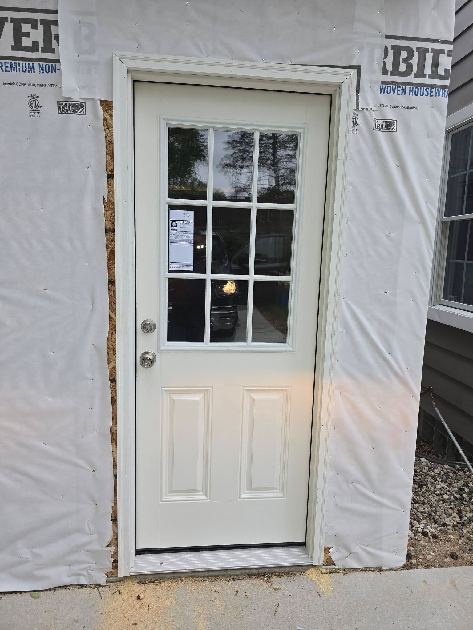 White exterior door with a window pane, taped sign, and construction wrap around the doorway