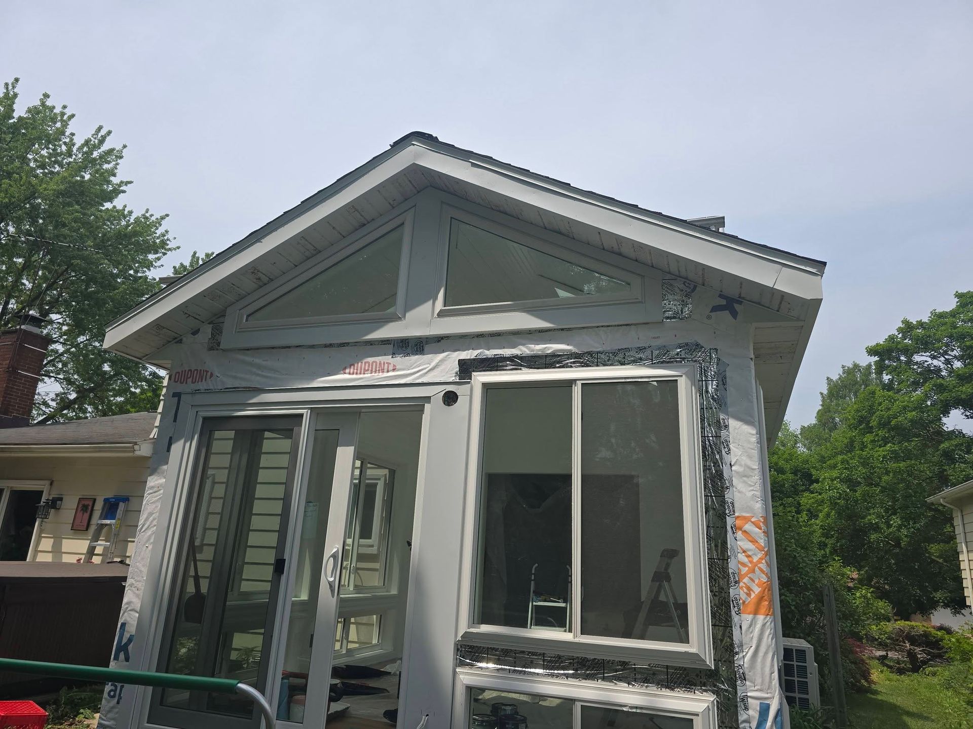 Small weathered gray house with a front porch and large windows under repair outdoors